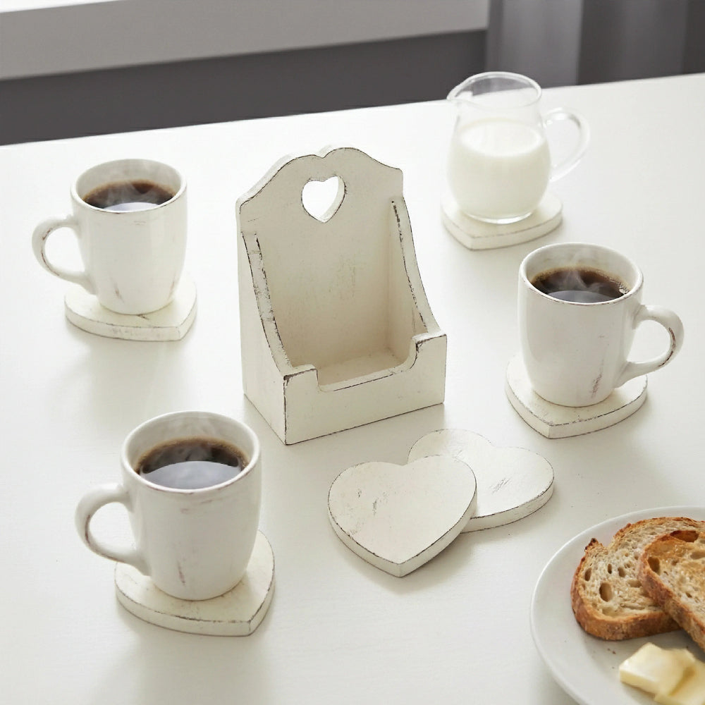 Three white mugs and a milk jar on heart coasters with an empty tall wooden holder and a plate of toast.