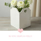 White decorative vase with heart cutouts holding white flowers on a wooden surface.
