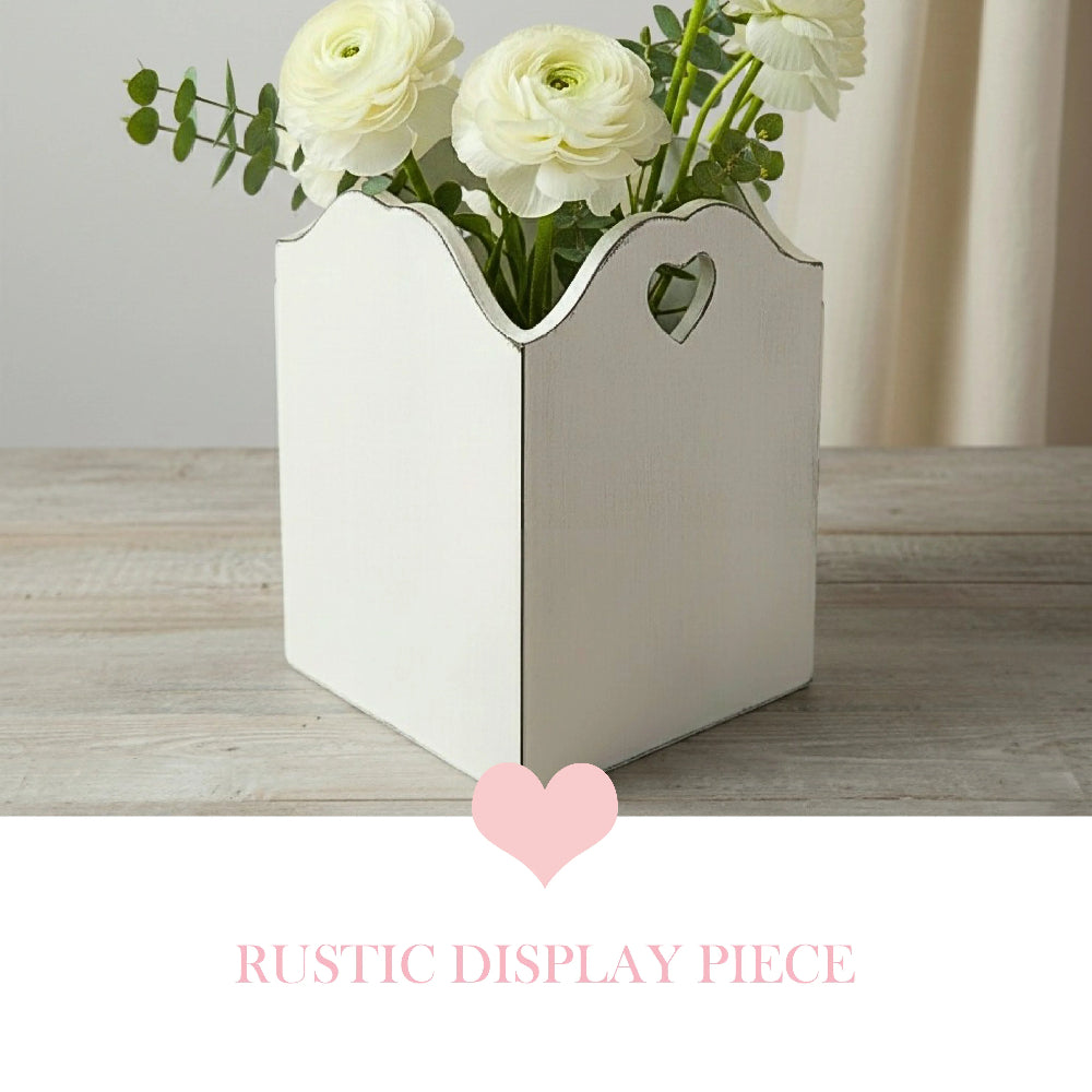 White decorative vase with heart cutouts holding white flowers on a wooden surface.
