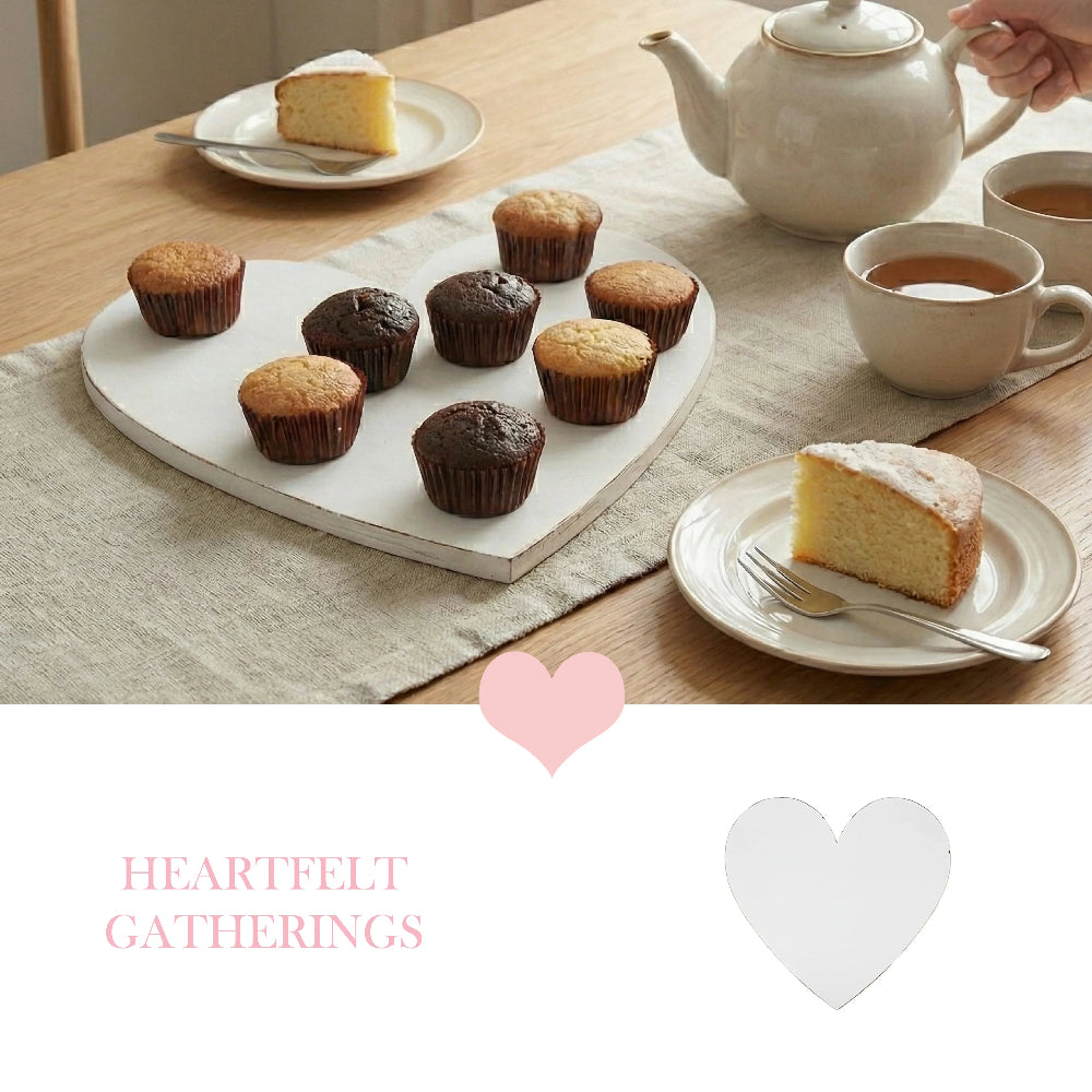 White heart-shaped tray holding nine muffins on a linen runner, with cake slices and tea on a light wooden table.