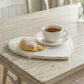 White heart-shaped wooden tray with a distressed antique finish, holding a powdered croissant on parchment paper and a white ceramic cup of tea on a rustic whitewashed table.