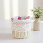 White wicker basket with floral lining and crochet lace trim on a white table next to small white flowers in a vase.