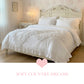 White ruffled bedding set on a carved cream headboard with floral wallpaper and a pink heart graphic below.