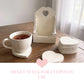 White tea cup on a heart coaster with a matching coaster stack and tall wooden holder on a rustic table with text.
