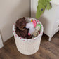 White wicker basket with floral lining filled with a teddy bear and stuffed toys on a wooden floor.