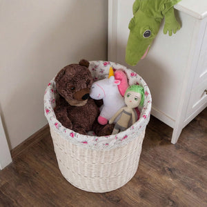 White wicker basket with floral lining filled with a teddy bear and stuffed toys on a wooden floor.