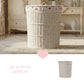 White wicker laundry basket with floral lining on a rug in a room with a console table and pink heart graphic.