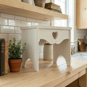 White wooden Countertop table with a heart cutout on a wooden surface and surrounded by books and plants.