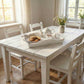 White wooden dining table with chairs in a bright room with natural light.