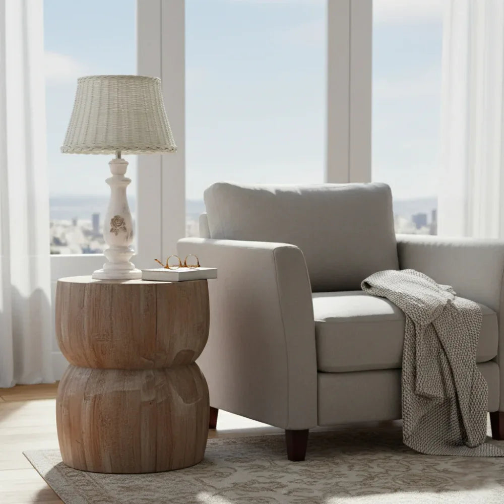 Living room with a beige armchair, wooden side table, and lamp near large windows.