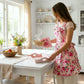Woman in a floral apron preparing food in a bright kitchen.