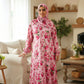 Woman wearing a pink floral dress and hijab in a living room setting.