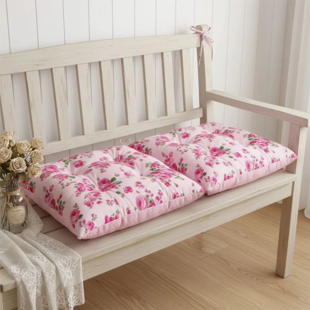 Wooden bench with pink floral chair cushions on a wooden floor.