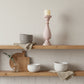 Wooden shelves with ceramic bowls, a wooden cutting board, and a candle on a neutral background