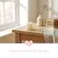 Wooden table with a antique White Pillar Candle, vase, and books in a bright room.